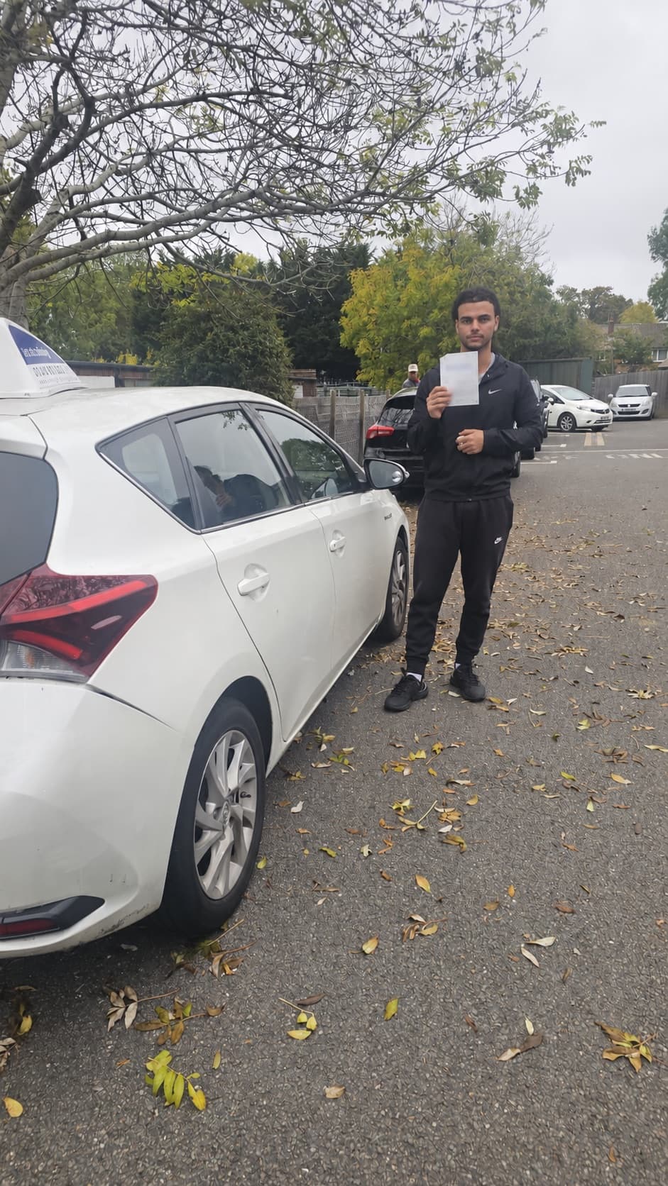 A pupil holding his pass certificate beside the Let's Go Driving car