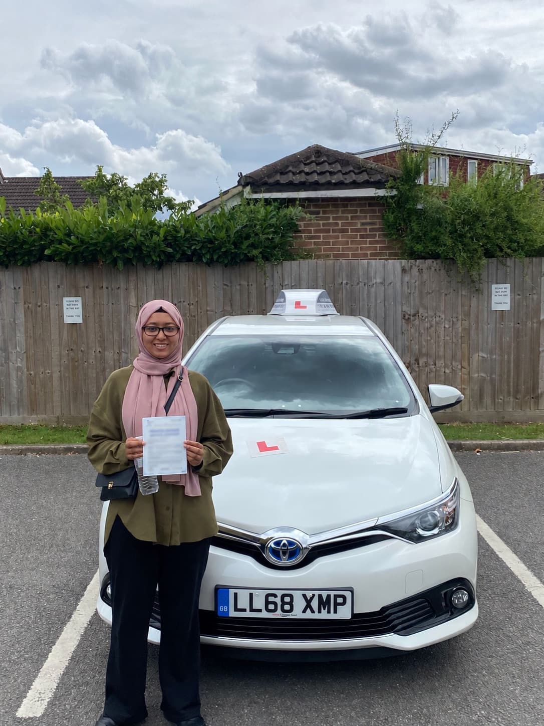 A pupil holding her pass certificate in front of the Let's Go Driving car