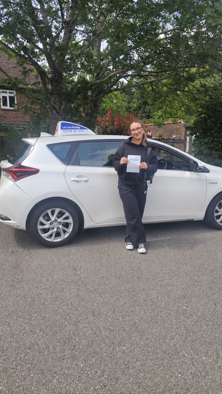A pupil holding her pass certificate beside the Let's Go Driving car