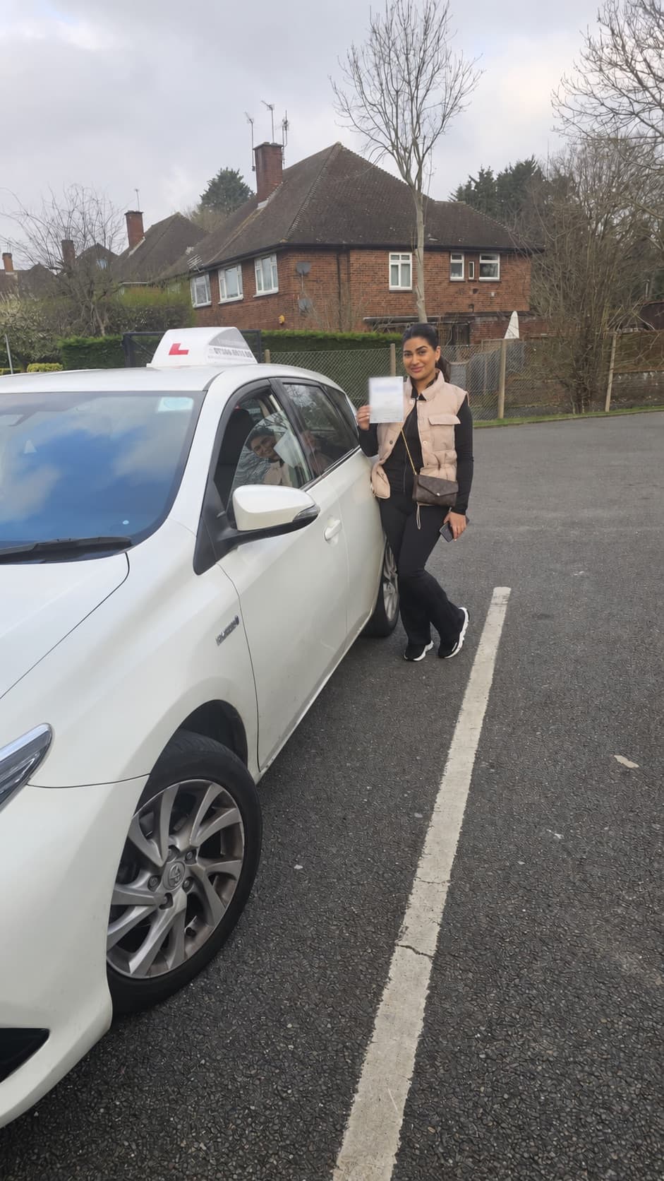 A pupil holding her pass certificate beside the Let's Go Driving car
