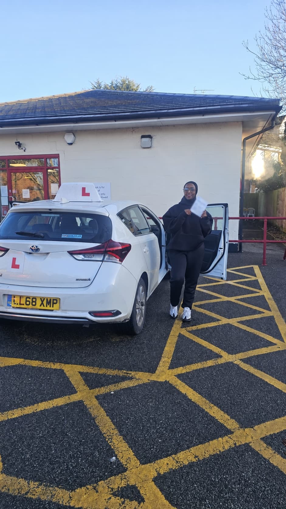 A pupil celebrating with her pass certificate beside the Let's Go Driving car